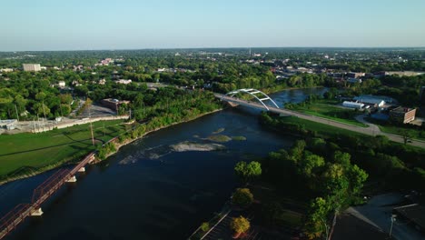 aerial drone shot a bridge gracefully spans over the river with driving cars, connecting suburban life on both sides with american houses surrounded urban naturein rockford, illinois with rock river