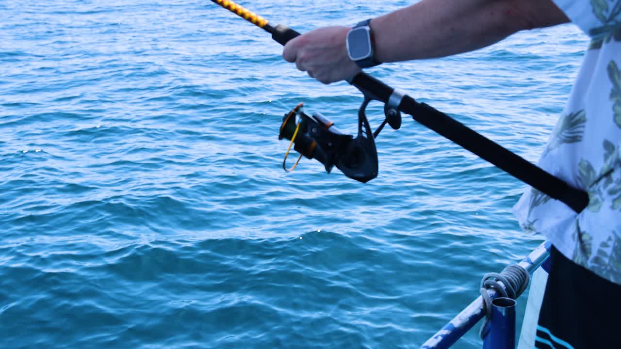 A person fishing from a boat in Phuket, Thailand, under bright daylight, capturing serene ocean views and focused angling