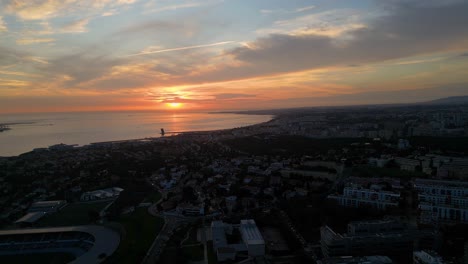 Luftaufnahme-Des-Sonnenuntergangs,-Blick-Auf-Die-Atmosphäre-Der-Goldenen-Stunde,-Sonnenstrahlen,-Die-In-Einem-Niedrigen-Winkel-über-Das-Wohngebiet-Der-Küstenstadt-Fallen