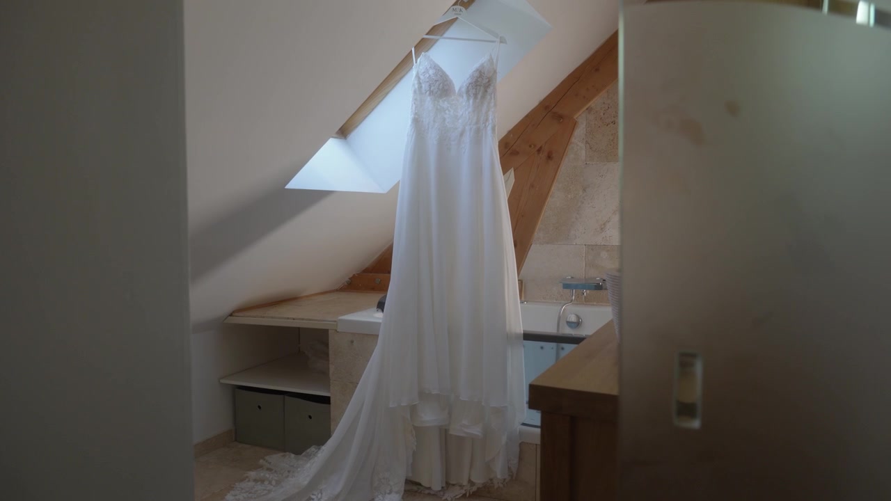 Camera Approach to White Wedding Dress Hanging in Bright Attic Room Bridal Preparation