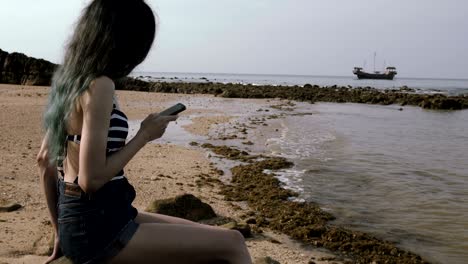 joven turista usando un teléfono móvil en la playa cerca del mar con un hermoso barco