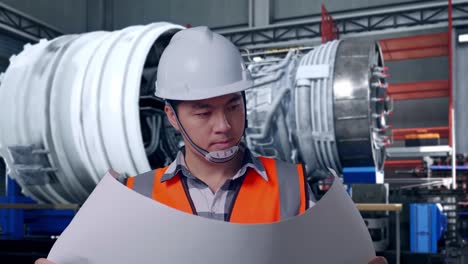 close up of asian male engineer with safety helmet looking at blueprint in his hands and looking around while standing with airplane engine maintenance conducted, analytics checking the turbine