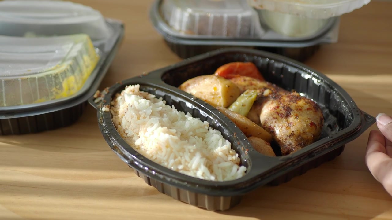 Person åbner plastik take away-beholder med stegt kylling og ris