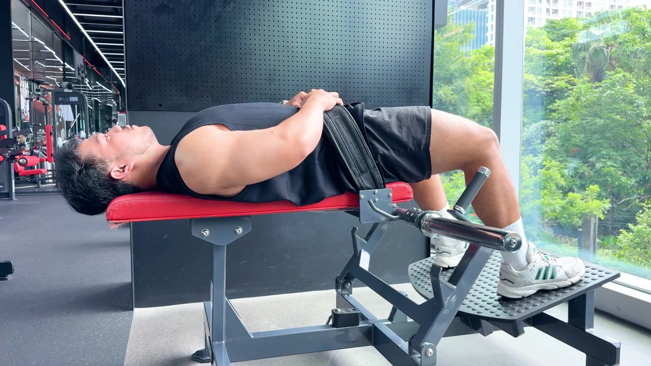 健壮男子在现代健身房的自然光下，于上斜凳上进行臀桥训练，侧面视角