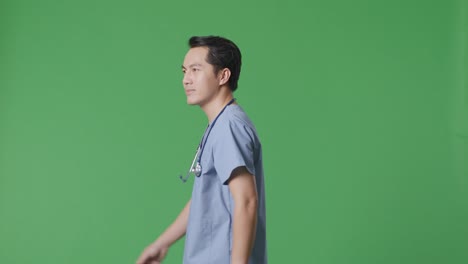 side view of asian male doctor with stethoscope looking around and walking on green screen background in the hospital