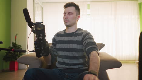 broadcast director adjusting camera with microphone in home studio, preparing for video shoot. camera gear and equipment are set up on table, getting ready for filming