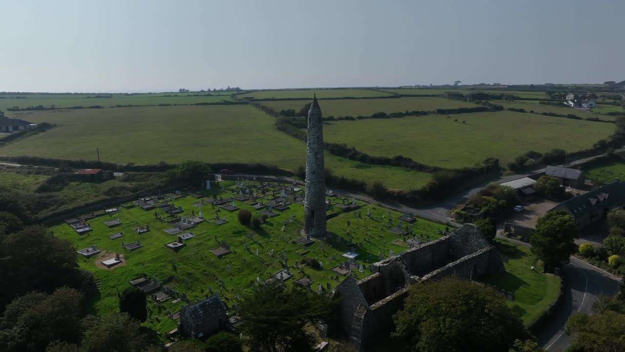 St. Declan's Monastery, Ardmore, County Waterford, Ireland, September 2024. Drone wide angle clockwise orbit around the Round Tower and graveyard separated by the leafy tree line on an overcast day.
