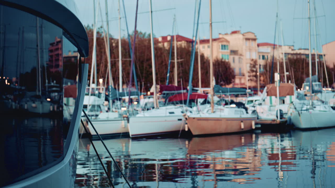 A yacht's bow in the foreground with the marina and boats in the background at blue hour
