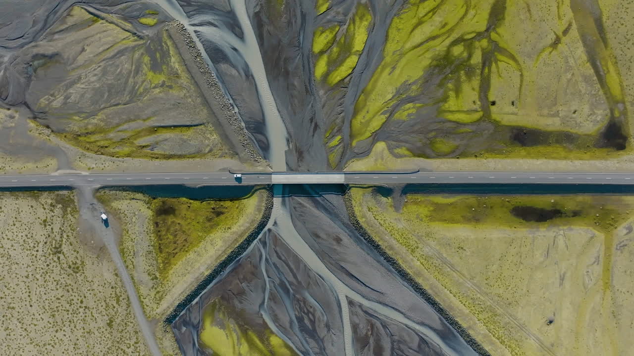 Top down drone shot of a car on a bridge driving over a river delta, in Iceland