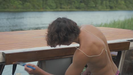 Young-topless-man-painting-sliding-door-overhang-on-wooden-boat-to-weather-seal