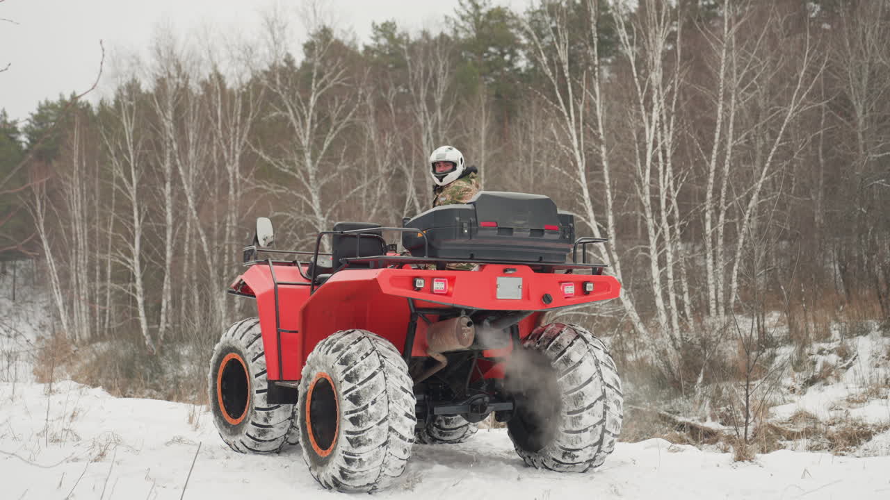 Quad rosso che sfreccia attraverso una foresta innevata, pilota che naviga su una pista ghiacciata, pneumatici che affondano nella neve, vapore di scarico che si alza, sfondo di betulle sotto un cielo nuvoloso, azione fuoristrada ad alta adrenalina e curve strette.