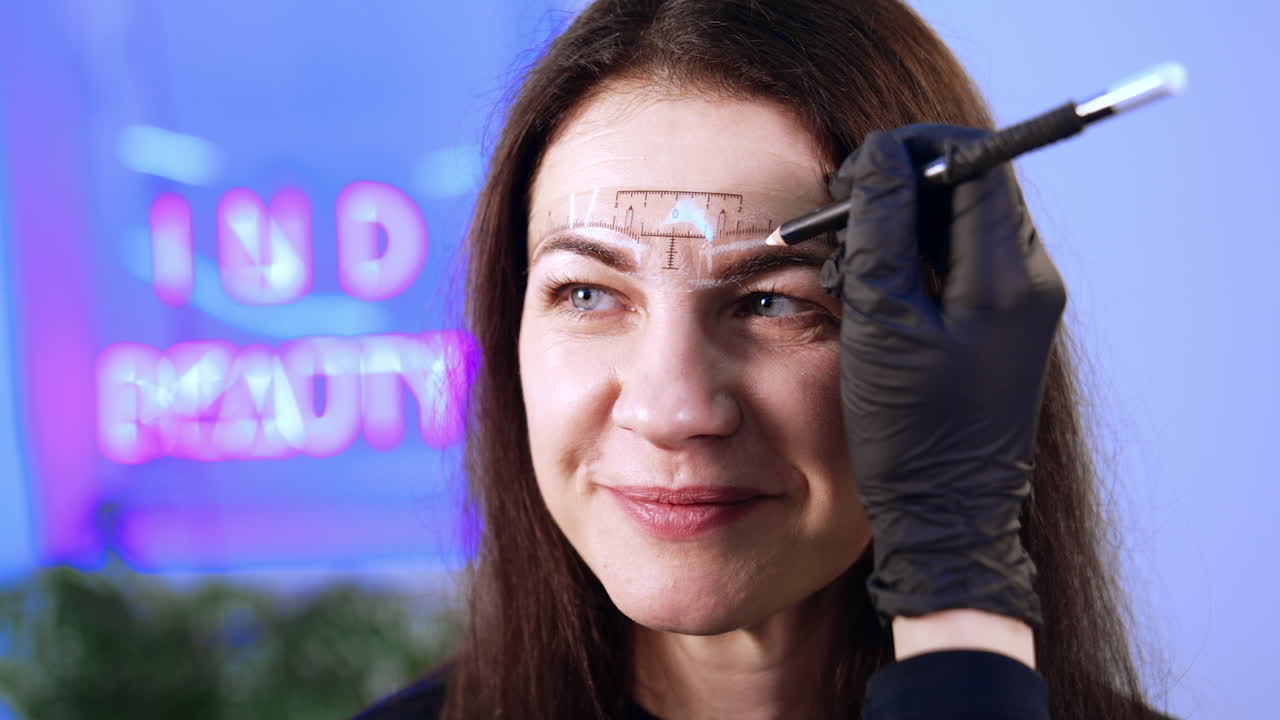 Special ruler is set on the female client's forehead. Beautician draws the lines with white pencil to mark the future eyebrow make up. Close up.
