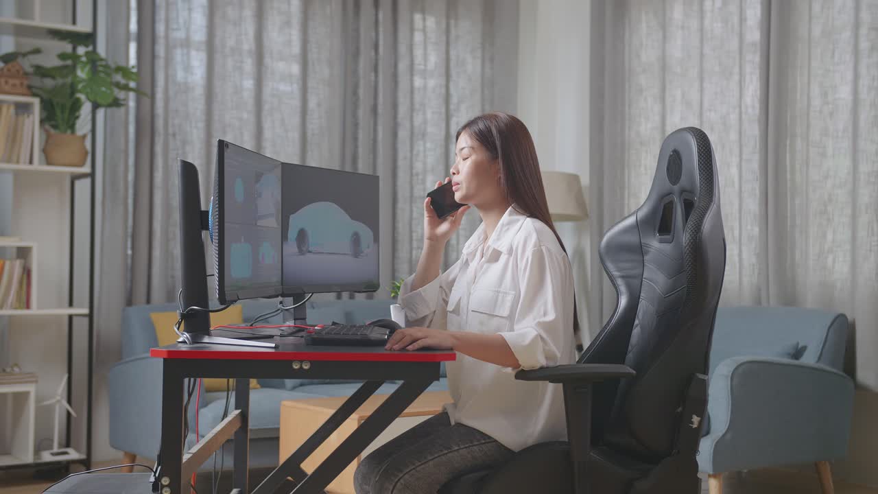 아시아 여성 자동차 디자이너가 스튜디오에서 데스크 컴퓨터에서 ev 자동차의 3d 모델을 작업하는 동안 스마트폰으로 이야기하는 측면 뷰