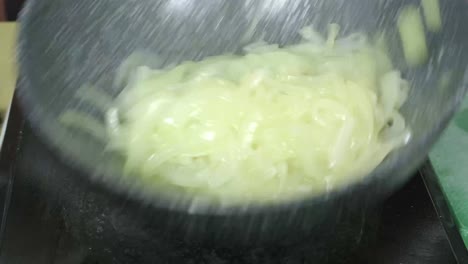una toma de primer plano de cebollas cortadas salteadas en una sartén siendo movidas por las manos del chef