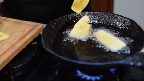 mujer friendo plátanos en una sartén con aceite