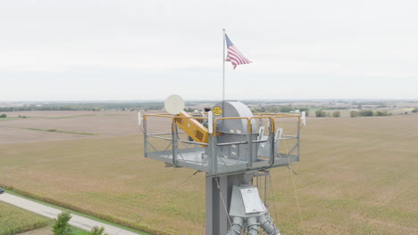 american flag flying atop an industrial tower over countryside farm fields, aerial