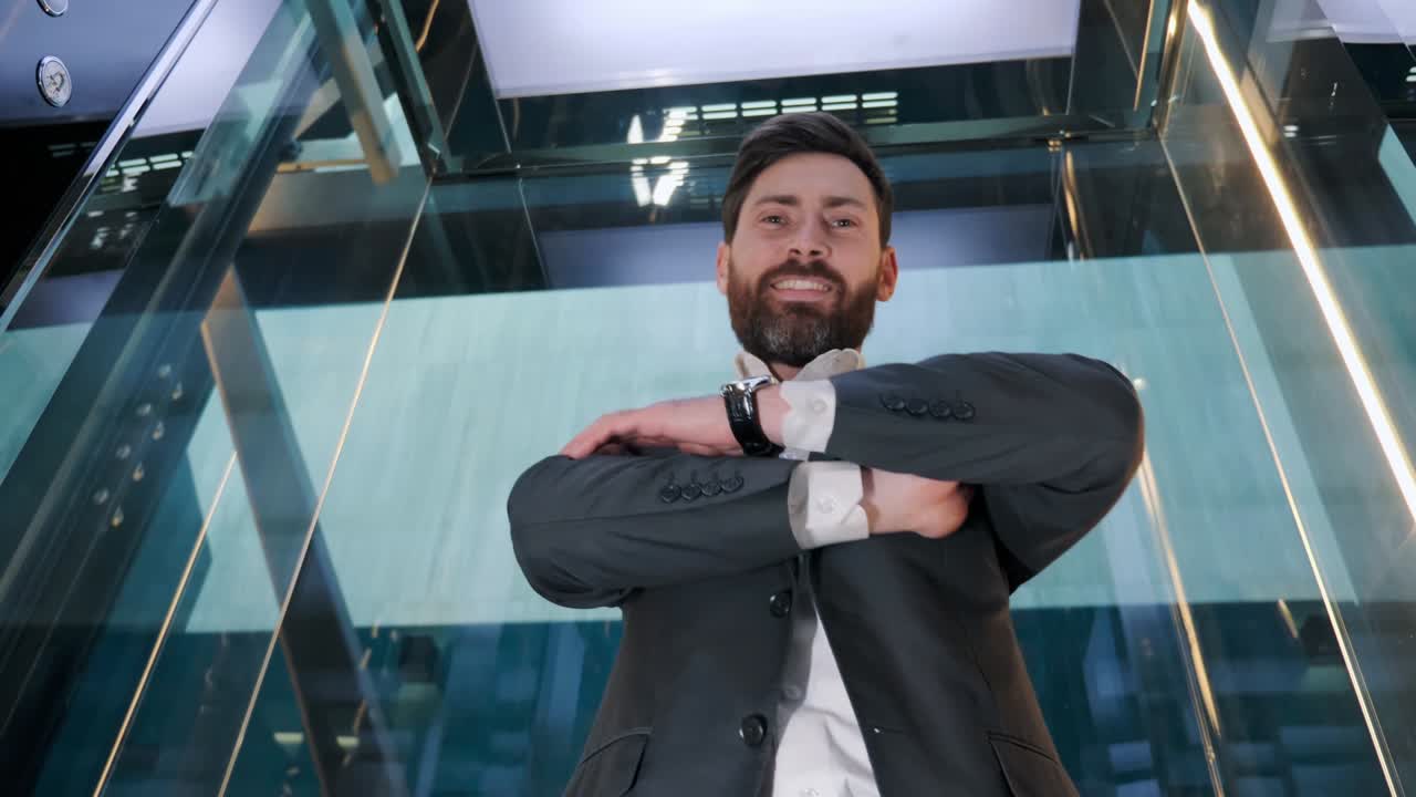 retrato de un exitoso hombre de negocios barbudo en un traje elevador de vidrio en movimiento en un centro de negocios moderno. hombre girando hacia la cámara, cruzando los brazos, sonriendo encantadoramente parece confiado.