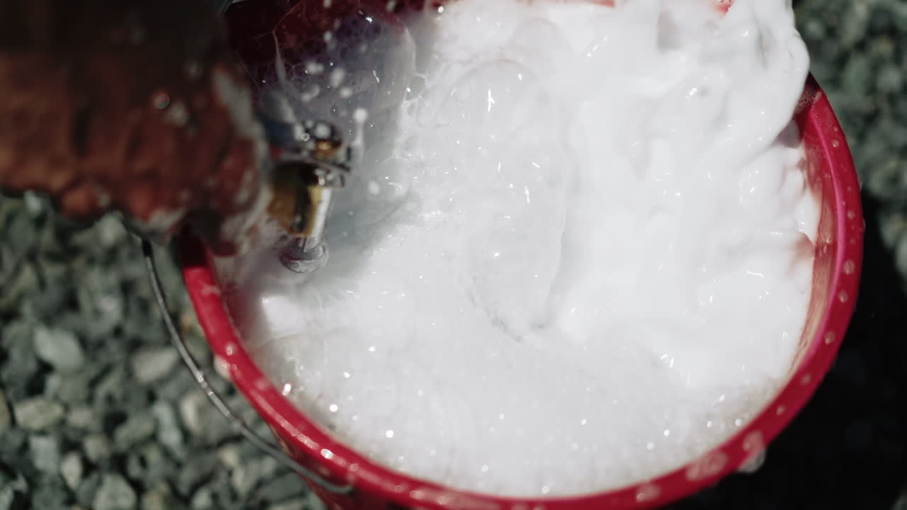 Close-up of a Person Washing with Soapy Water in a Red Bucket
