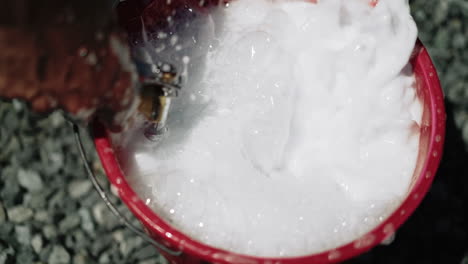 close-up of a person washing with soapy water in a red bucket