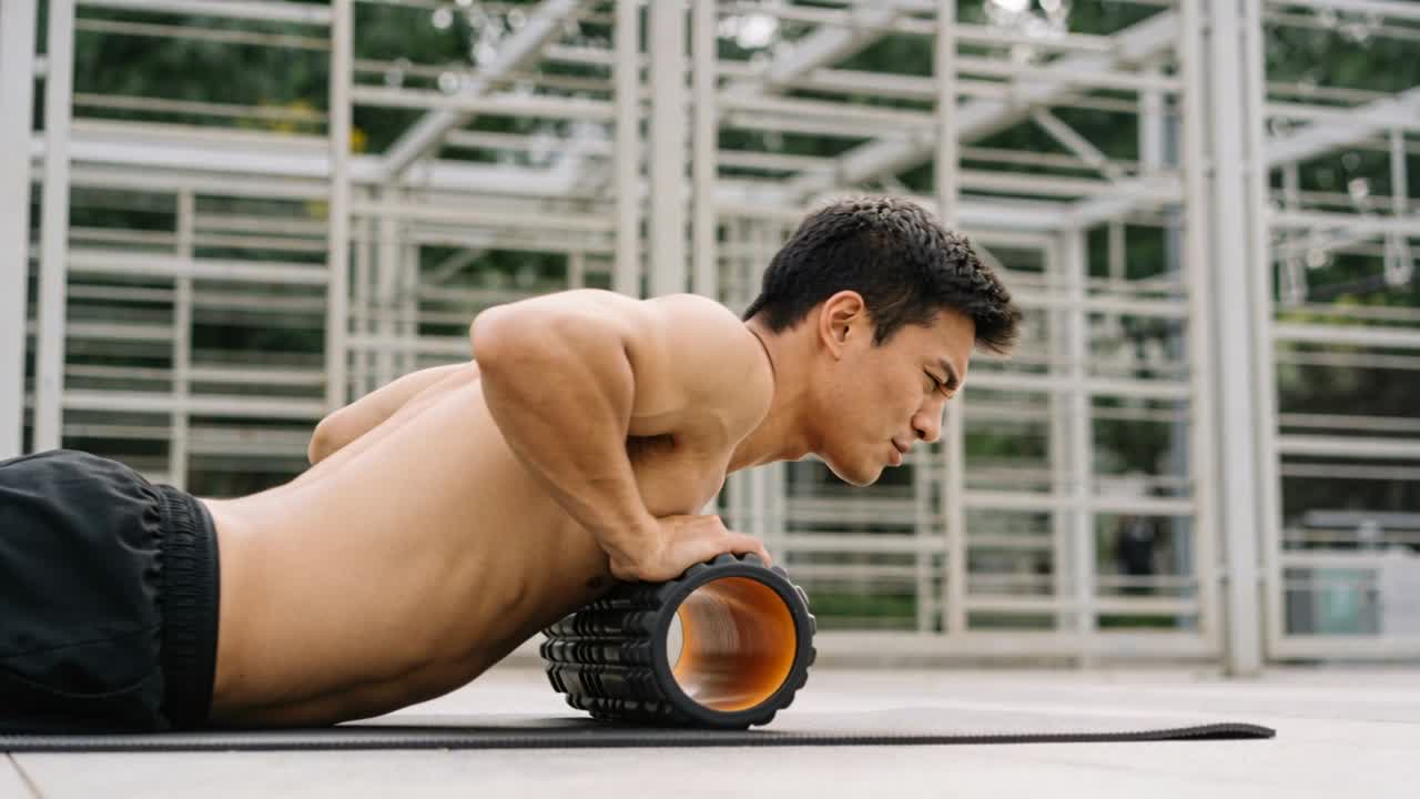 Bracing hands on foam roller, shirtless male rolling chest for tissue release on rooftop scaffold