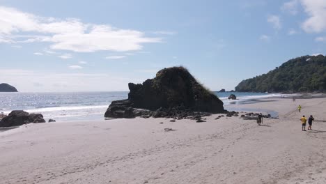 aerial-drone-shot-on-a-white-sandy-beach-rising-over-a-rock-towards-the-ocean