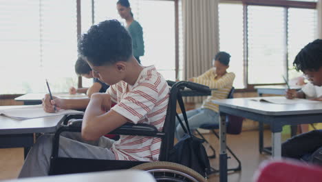 in school, boy in wheelchair writing in notepad in classroom setting
