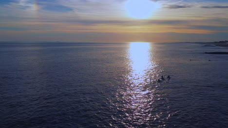cámara de dron nivelada a baja altitud retira la toma de carro con una puesta de sol dorada a la vista - surfistas debajo esperando la ola perfecta