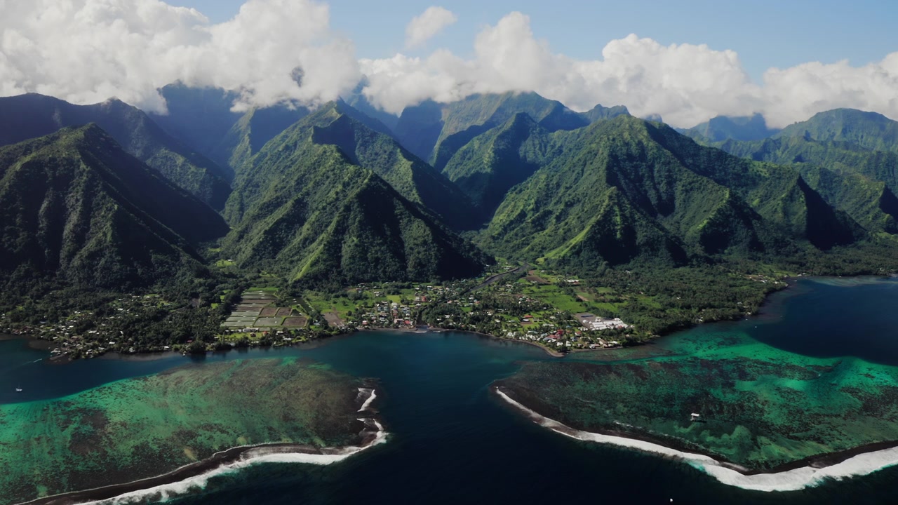 Ilmakuva dronella Teahupoon riutasta ja rannikosta, Tahitilla, sademetsän huiput kehystävät turkoosia vettä hajanaisten iltapäiväpilvien alla