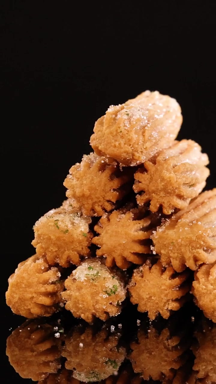 Et stramt vertikalt bilde av sukkerbelagte churros som roterer på en reflekterende svart bakgrunn.
