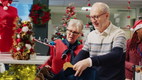 Older-client-browsing-through-festive-ornate-clothing-store-racks-with-wife-in-Christmas-shopping-spree.-Senescent-couple-searching-for-stylish-outfit-as-present-for-nephew-during-holiday-season