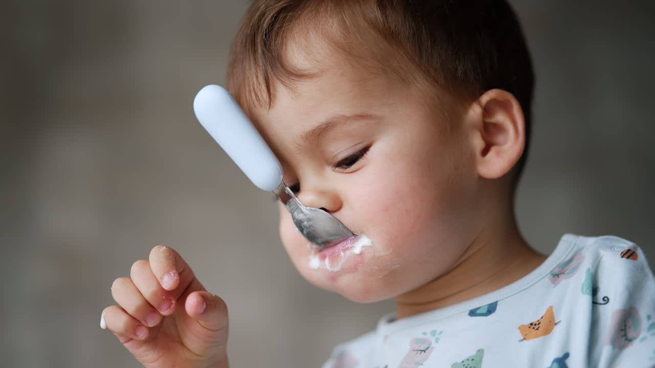 Funny Caucasian kid with a spoon in his mouth. Close up. Portrait of a kid with yoghurt all over his face.
