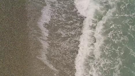 calm ocean waves from above with a top down view over a pebbled beach in looc bay, philippines