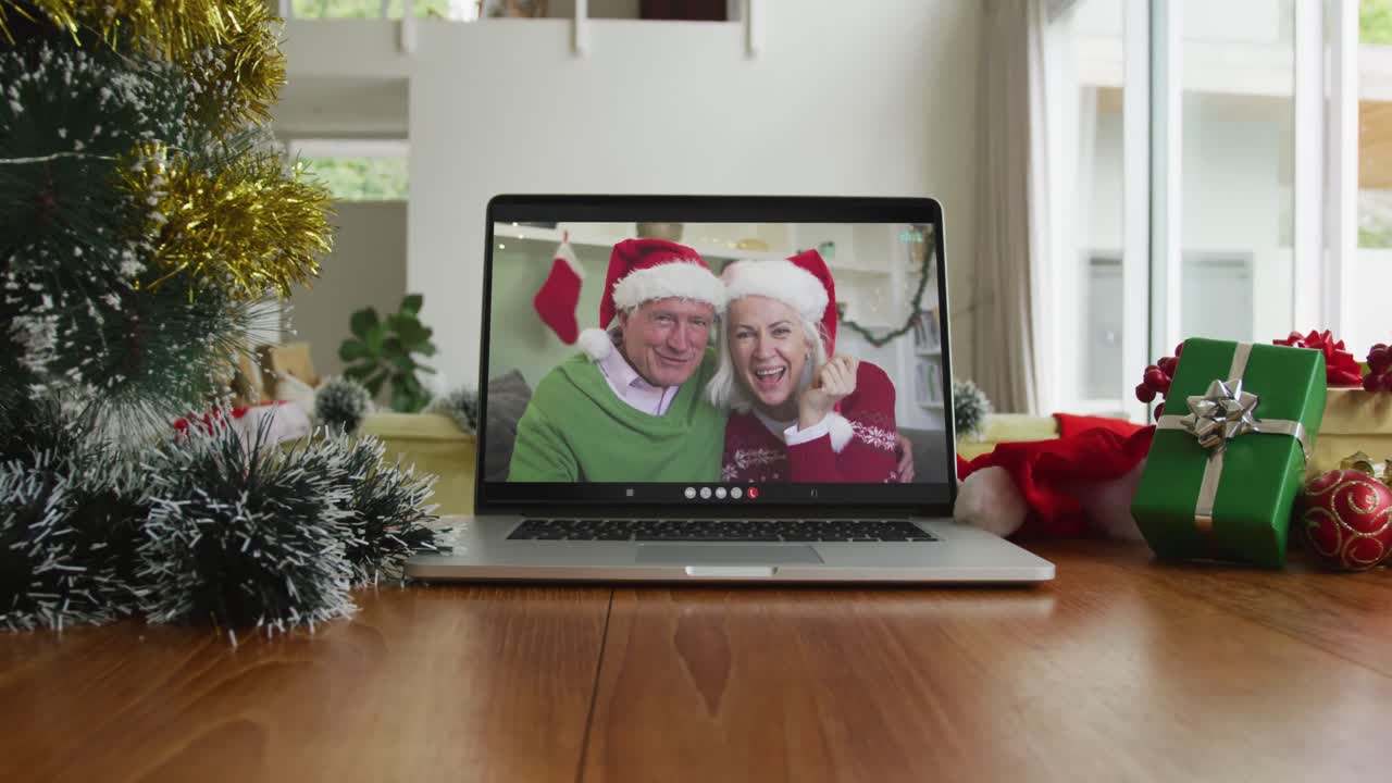 una pareja caucásica de alto nivel sonriente con sombreros de santa en una videollamada de navidad en una computadora portátil