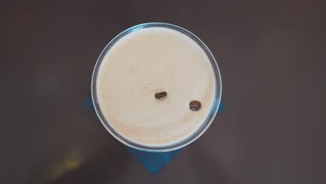 hand placing three coffee beans on to foam of espresso martini, top down