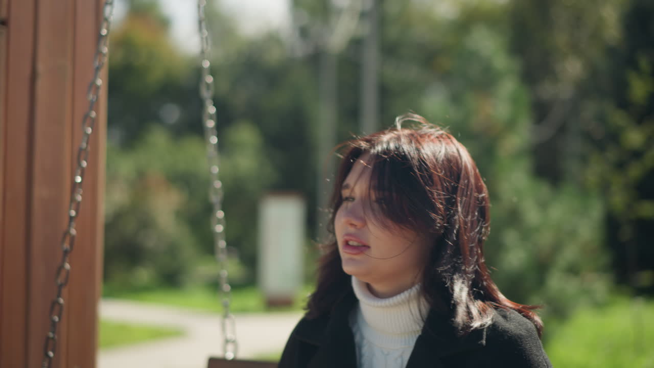 나무로 된 스에 앉아있는 여자의 친밀한 클로즈업, 그녀의 머리카락은 부드럽게 바람에 불어, 울창한 초록색의 조용한 배경