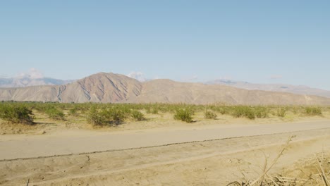 Una-Toma-Panorámica-Que-Muestra-Una-Carretera-Abandonada-En-Medio-Del-Desierto-Rodeada-De-Montañas-En-Un-Día-Soleado