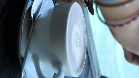 Vertical-shot-of-a-delicious-coffee-latte-from-bali-indonesia-with-the-beautiful-blue-sea-in-the-background-being-drunk-and-enjoyed-during-a-break-from-traveling