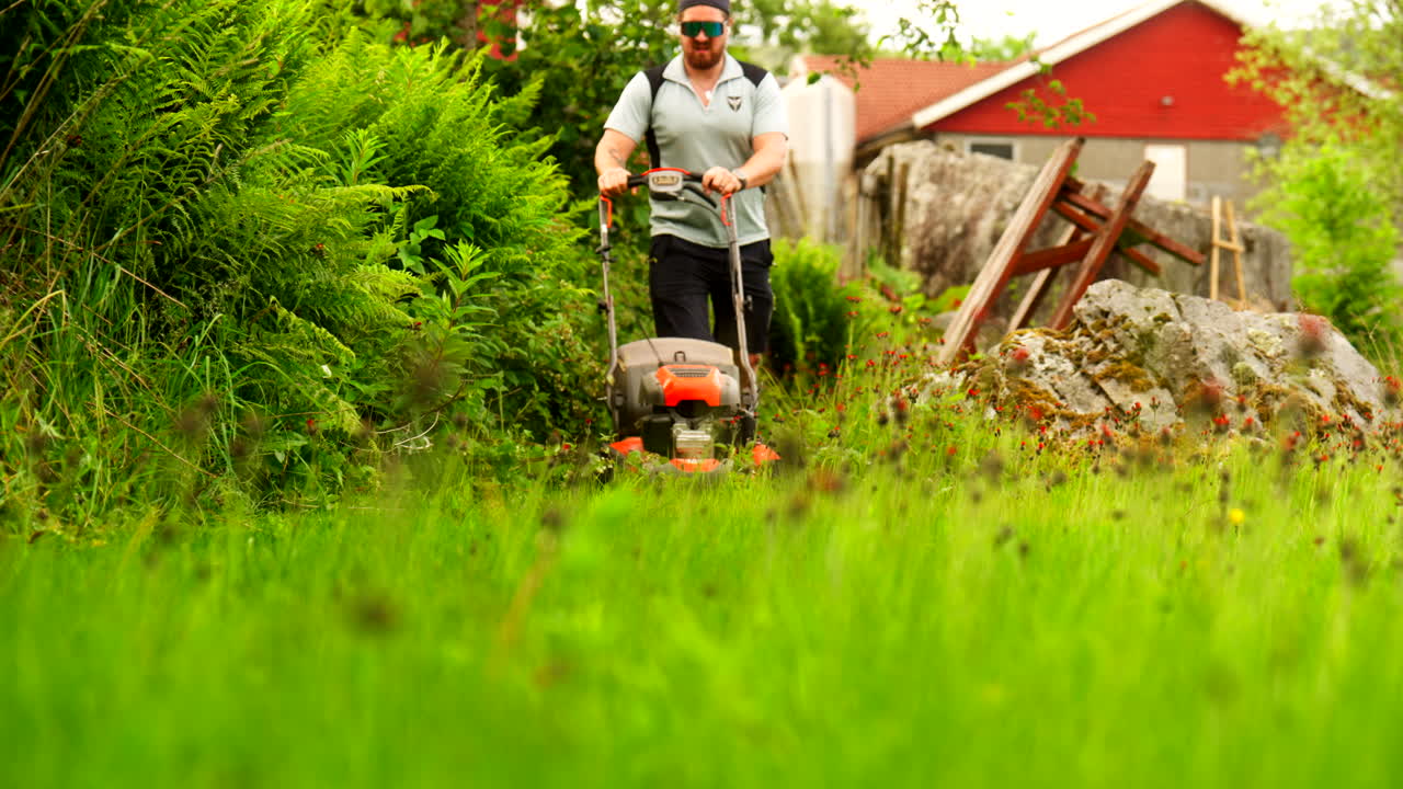 Young man strimming overgrown grass in a rural garden with ferns and rubble in foreground, showcasing outdoor maintenance and gardening work