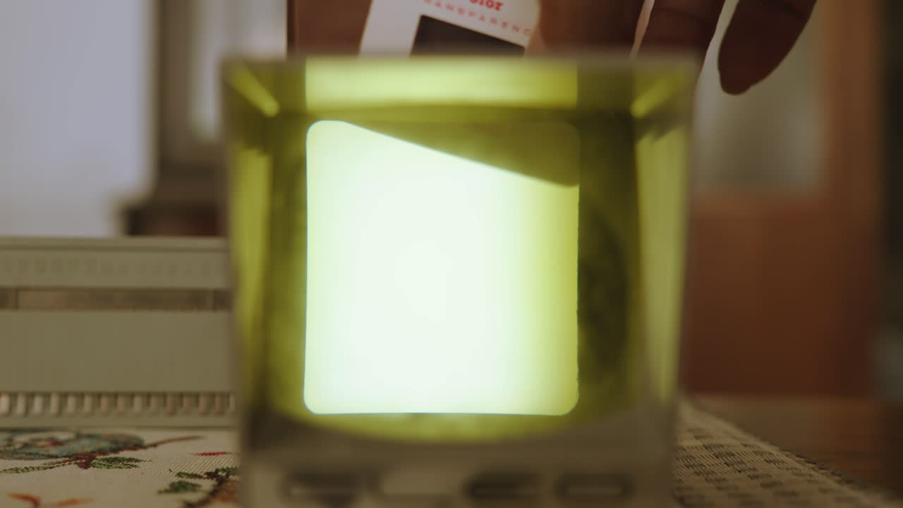 A person's hand inserts diapositives into a small projector