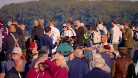 Diverse crowd of people gathers at Airborne Ede, Ginkelse Heide, enjoying the event on a sunny day. Attendees, ranging from families to veterans, move around and chat in a vibrant atmosphere