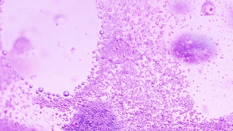 foto macro de muchas pequeñas burbujas violetas brillando en el agua y una gran burbuja cayendo al suelo desenfocada con un fondo brillante