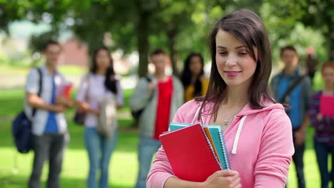 estudiante sonriendo a la cámara con amigos de pie detrás de ella en el césped