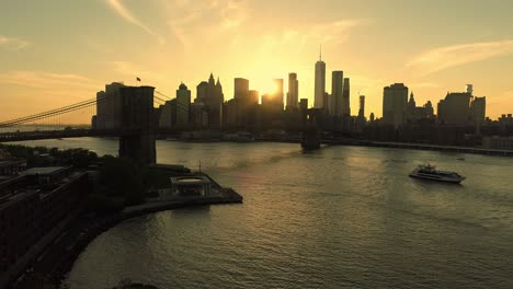 Puente-De-Brooklyn-Sobre-El-Río-Hudson-Y-Puesta-De-Sol-Dorada-Detrás-Del-Horizonte-De-Manhattan,-Nueva-York