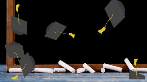 multiple graduation hats falling against wooden slate and chalks over wooden surface