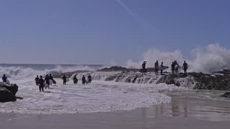 surfers with surfing boards watching powerful waves breaking on rock formation at snapper rocks, qld, australia. wide shot
