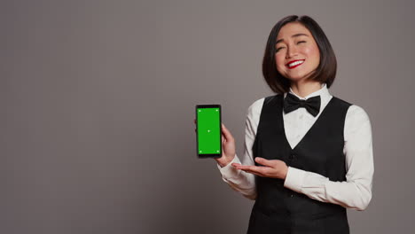 Asiatischer-Hotel-Concierge-Zeigt-Auf-Telefon-Mit-Greenscreen-Layout