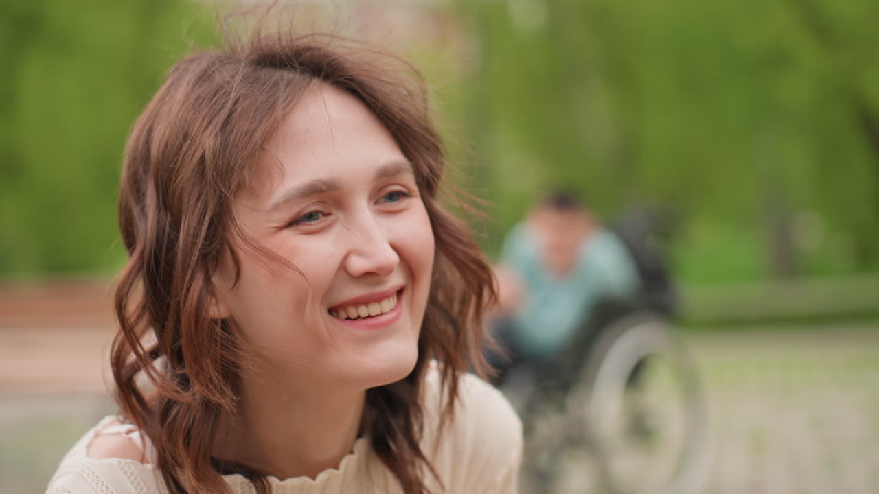 White Woman Smiling Near Wheelchair In Green Park Portrait With Joyful Expression And Candid Gaze Soft Sunlight, Casual Denim In Background And Inclusive Scene Highlighting Connection And Hope