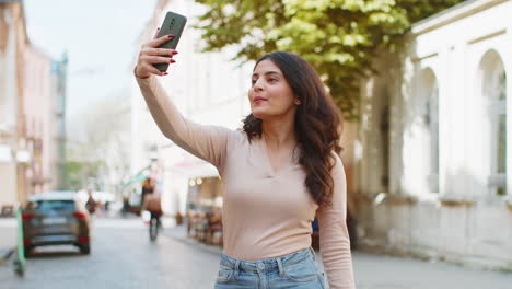 Indian-woman-blogger-taking-selfie-on-smartphone-video-call-online-with-subscribers-on-city-street