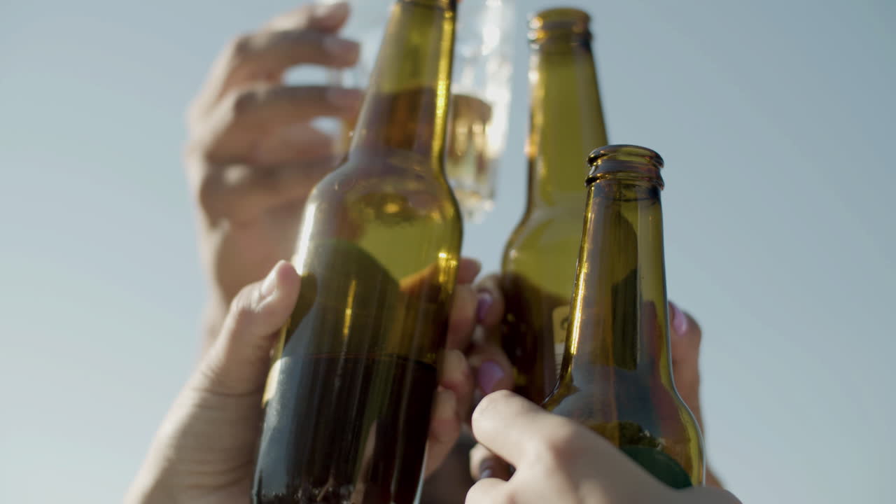 primer plano de amigos irreconocibles levantando y tintineando botellas de cerveza