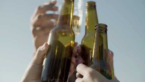 primer plano de amigos irreconocibles levantando y tintineando botellas de cerveza